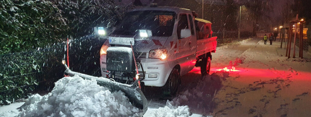 Winterdienst - ein kleines Winterdienstfahrzeug schiebt Schnee auf einem Gehweg.