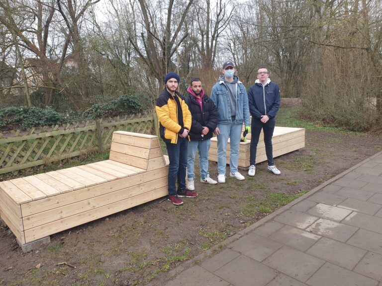 Vier junge Männer stehen vor ihren selbst gebauten Liegepodesten aus Holz, die sie kurz vorher am Platz der Generationen selbst aufgebaut haben.