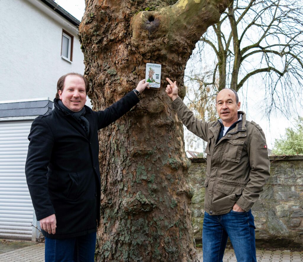 Martin Burlon, Erster Stadtrat Dreieich und Sylvio Jäckel, Baumexperte DLB stehen vor einem Habitatbaum und zeigen auf das Schild.